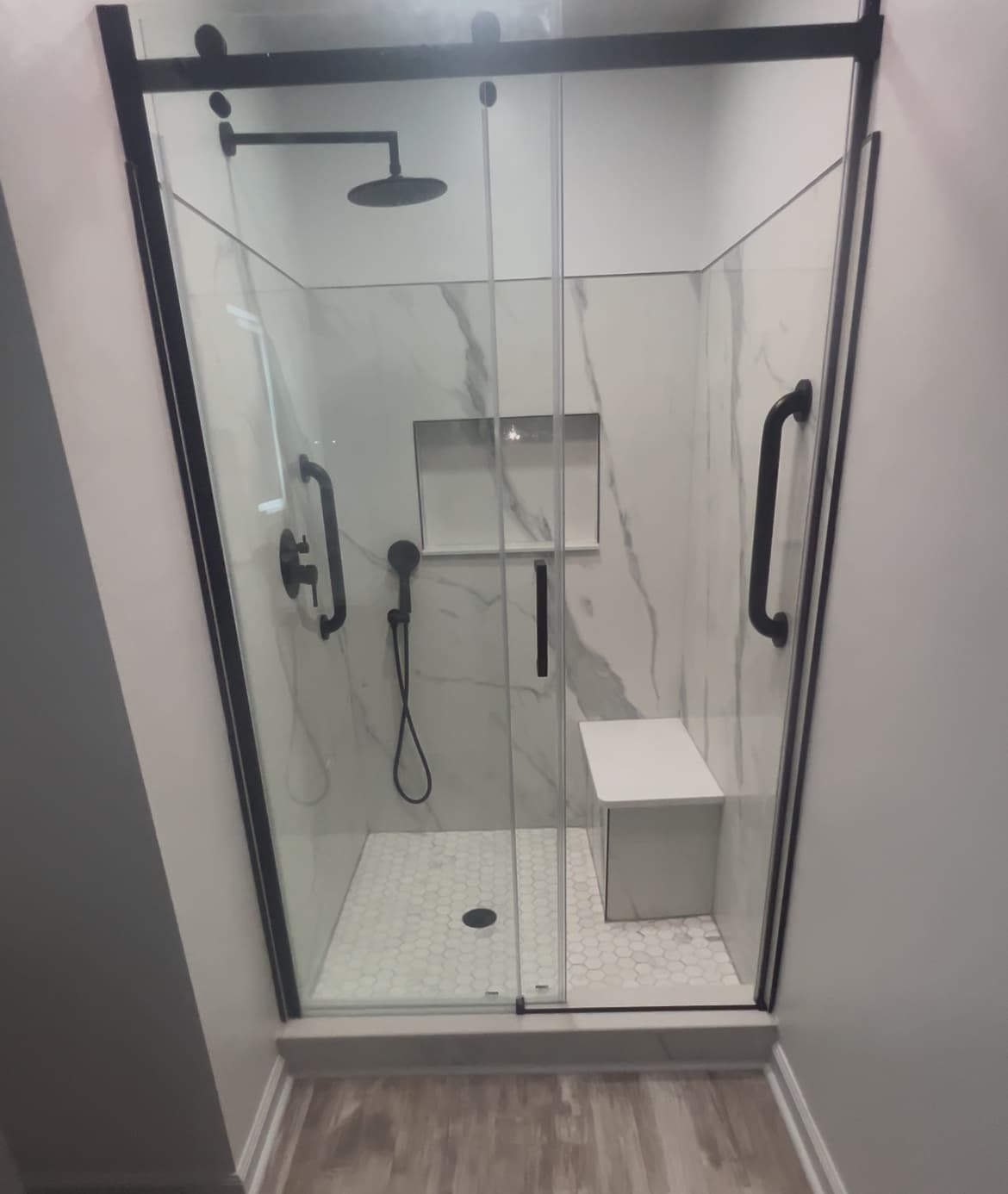 Finished walk-in shower with marble walls, black fixtures, and hex tile floor